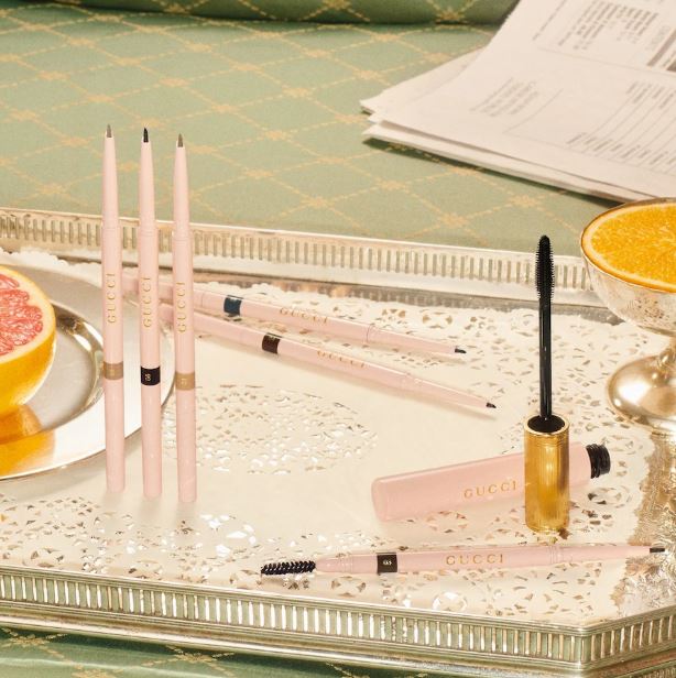 Makeup products including brushes and a mascara on a decorative tray with a green checkered tablecloth.
