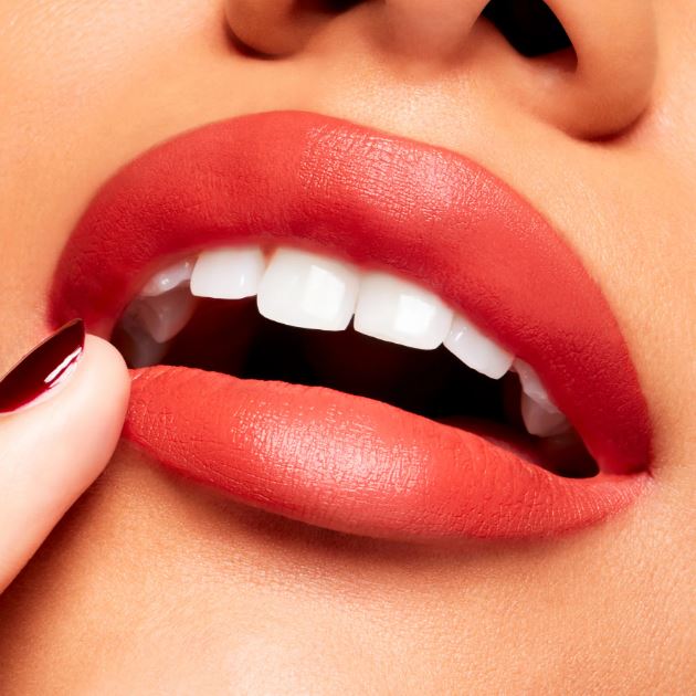 Close-up of a person applying red lipstick to their lips.