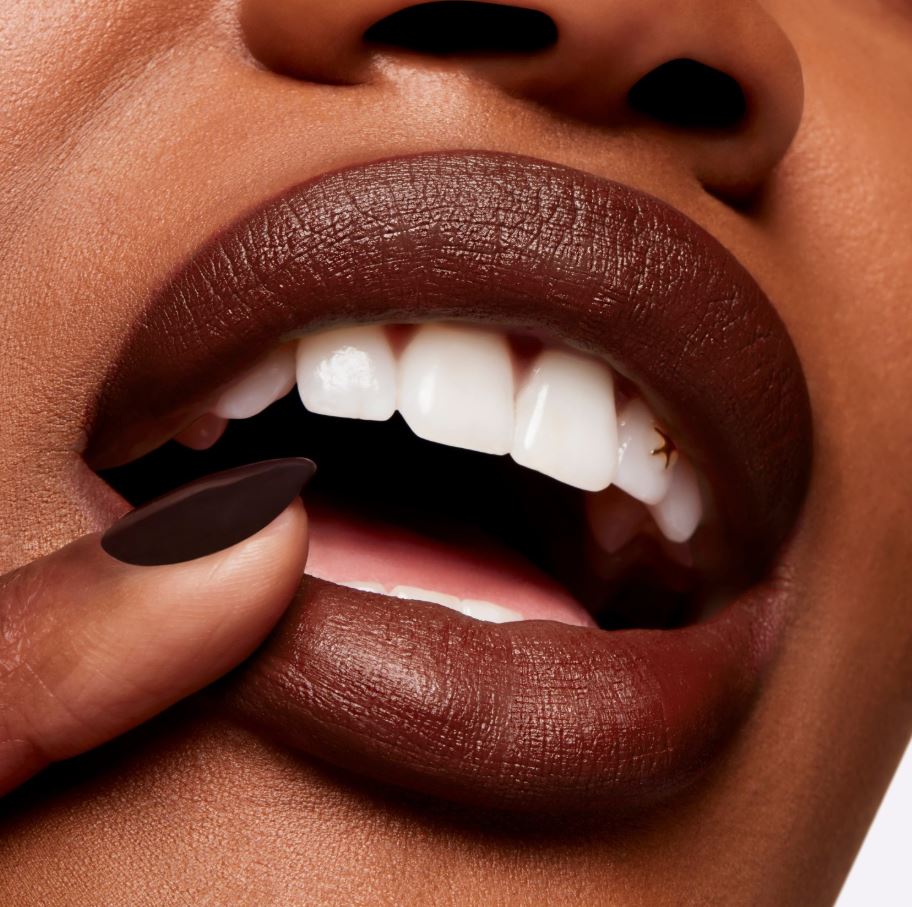 Close-up of a person's mouth with dark lipstick and a hand touching the lips.