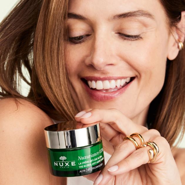 Woman holding a Nuxe skincare product with a neutral background