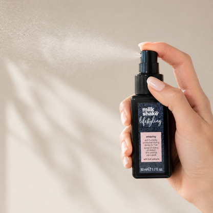 Hand holding a bottle of 'milk shake' hair product against a neutral background