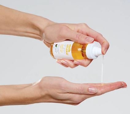 Hand holding a bottle of oil with a dropper, pouring it into another hand against a light background