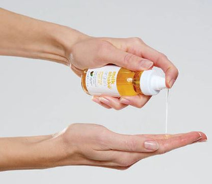 Hand holding a bottle of oil with a dropper, pouring it into another hand against a light background
