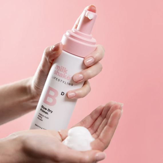 Hand holding a 'milk shake Lifestyling' product with a pink cap against a pink background
