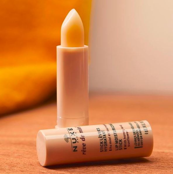 Nuxe lip balm on a wooden surface with a blurred background