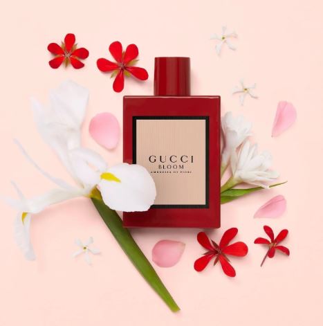 Gucci Bloom perfume bottle surrounded by flowers on a pink background