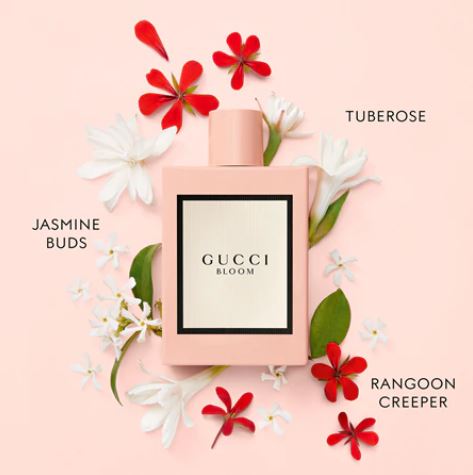 Gucci Bloom perfume bottle surrounded by flowers on a pink background