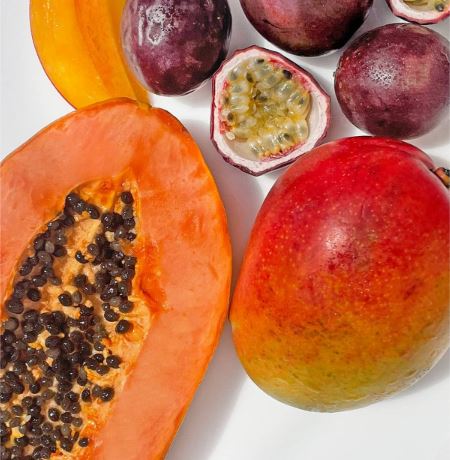 Assorted tropical fruits including a papaya, mango, and passion fruit on a white background