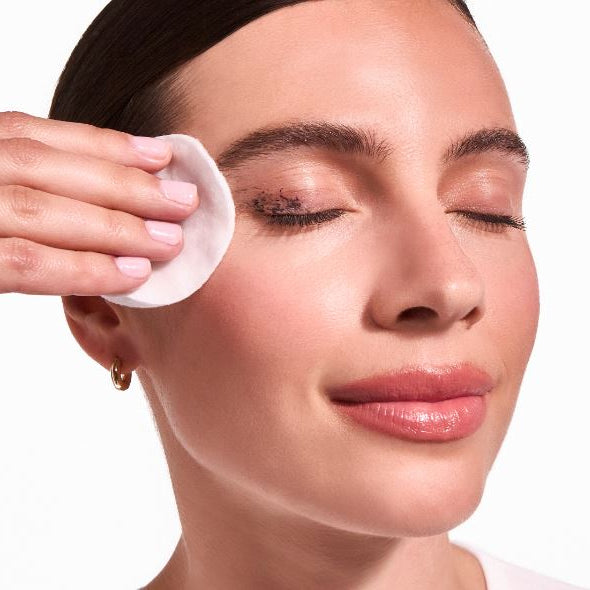 Woman applying a skincare product to her face with a cotton pad.