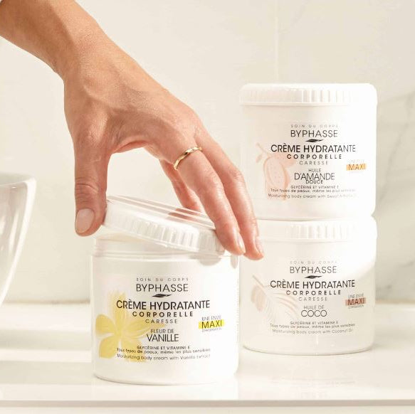 Two containers of Byphasse hydrating body cream with a hand reaching towards one of them.