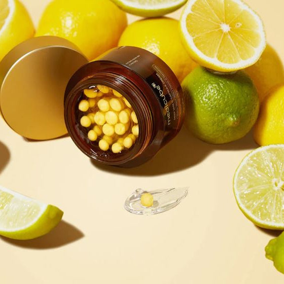 Open jar of yellow capsules with lemons and limes on a light background