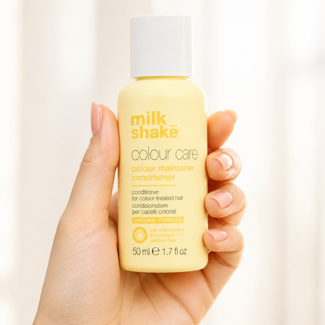 Hand holding a bottle of milk shake colour care conditioner against a plain background