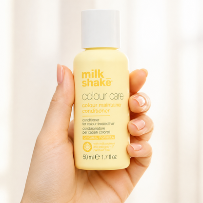 Hand holding a bottle of milk shake colour care conditioner against a plain background
