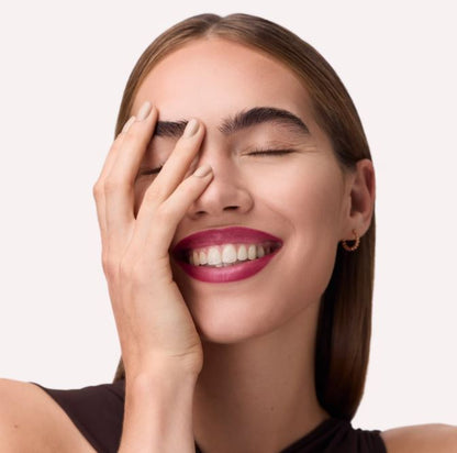 Woman with a bright smile and hand on face against a plain background