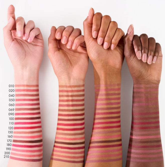 Four hands with different skin tones displaying swatches of a makeup product on their arms.