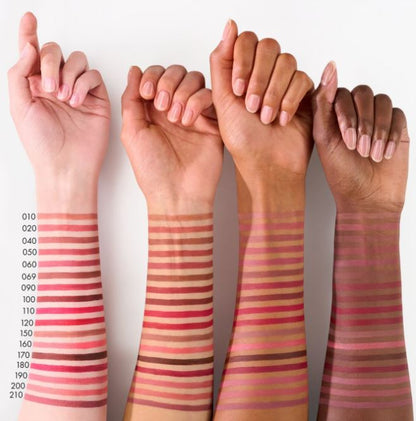 Four hands with different skin tones displaying swatches of a makeup product on their arms.