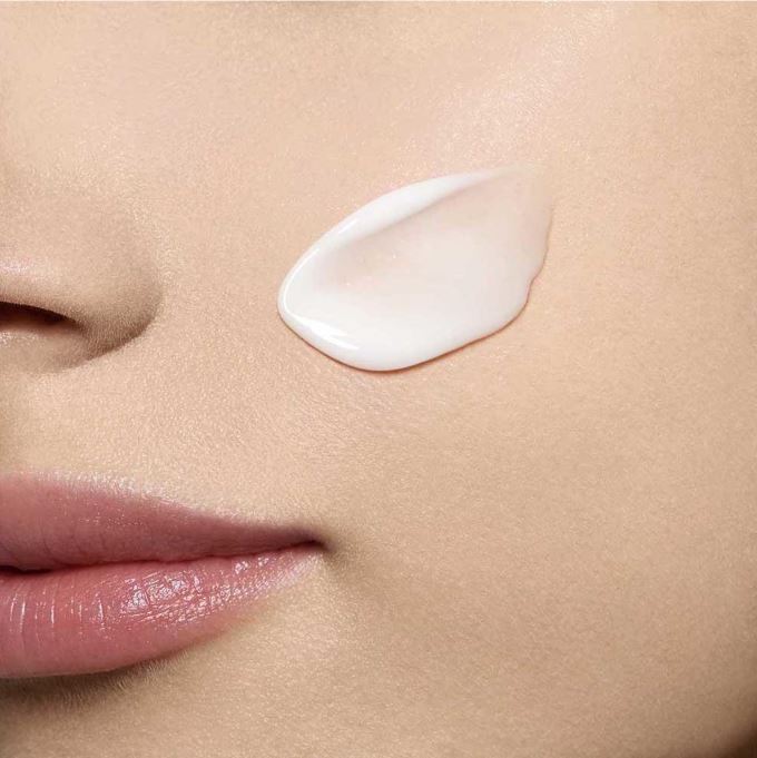 Close-up of a woman's face with a droplet of white cream on her cheek