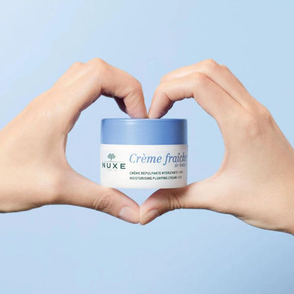 Nuxe Crème fraçìhe jar held between hands against a light blue background