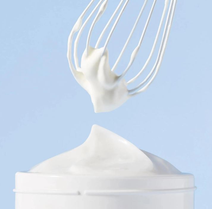 White whisk with whipped cream over a white container against a light blue background