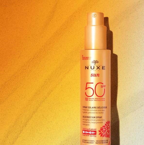 Nuxe sun spray bottle with SPF 50 on a yellow textured background