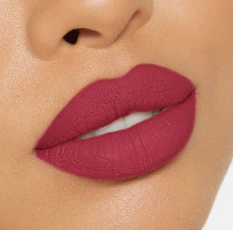 Close-up of a person wearing a vibrant pink lipstick on a neutral background