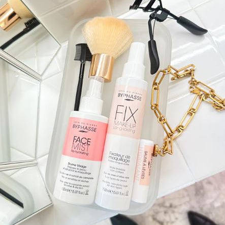 Cosmetic products including bottles and a brush on a white surface with a mirror in the background.
