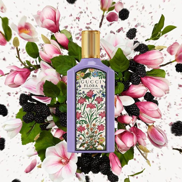Perfume bottle with floral design surrounded by pink flowers and blackberries