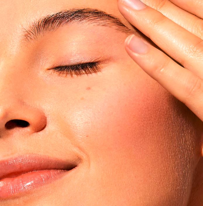 Close-up of a person's face with a hand on their forehead, focusing on skin texture.