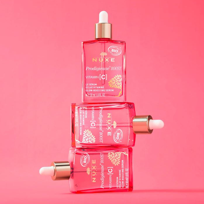Three Nuxe skincare bottles stacked on a pink background