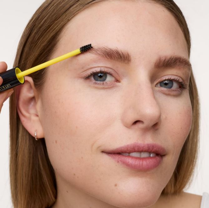 Woman applying eyebrow gel with a brush to her eyebrows.