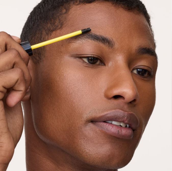 Person using a yellow and black eyebrow pencil on their face against a white background
