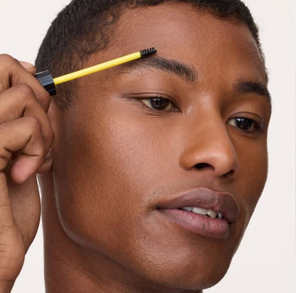 Person using a yellow and black eyebrow pencil on their face against a white background
