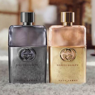 Two Gucci perfume bottles, one silver and one gold, on a textured surface.