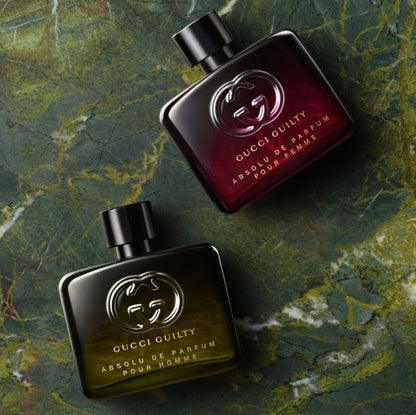Two Gucci Guilty perfume bottles on a textured green surface