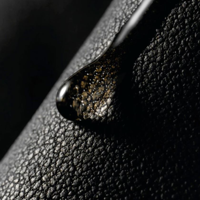 Close-up of a black leather surface with a droplet of water and dirt.