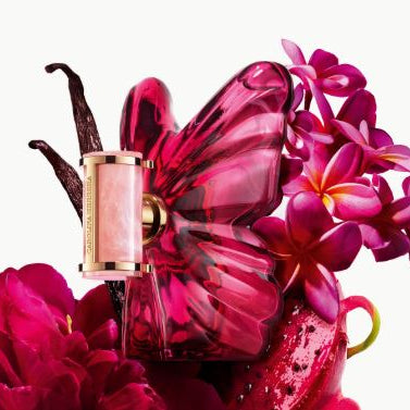 Pink butterfly-shaped perfume bottle with flowers and vanilla bean on a white background