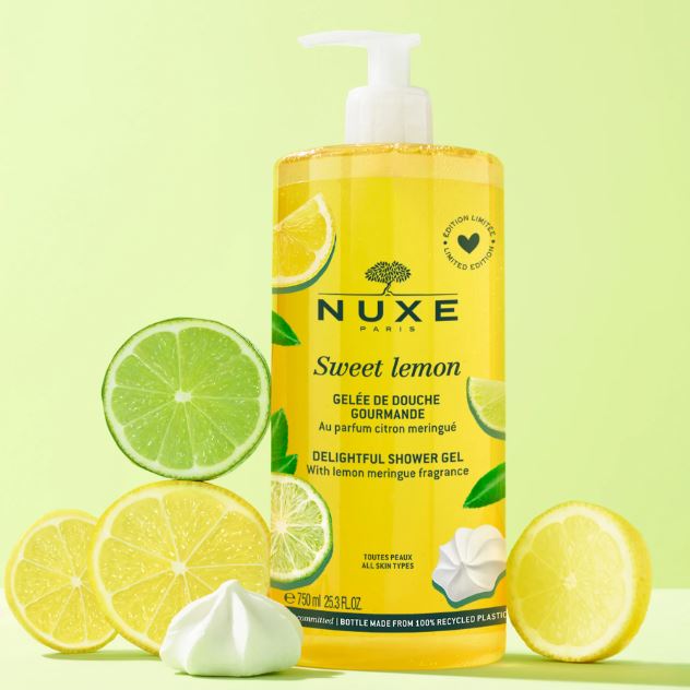 Nuxe Sweet Lemon shower gel bottle with lemons and lime slices on a light green background