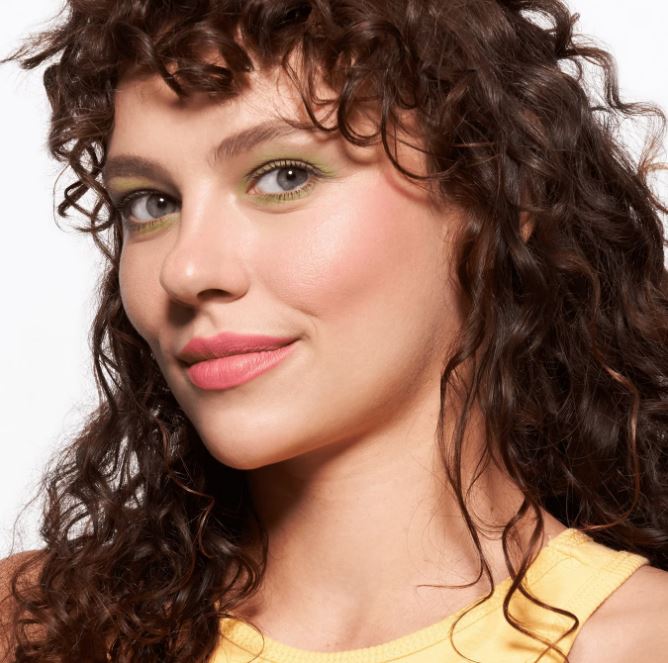 Woman with curly hair wearing a yellow top against a white background