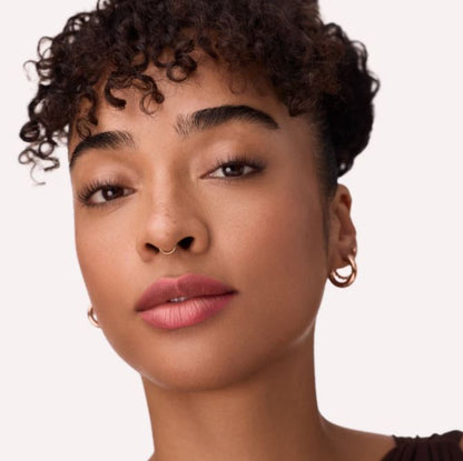 Close-up of a woman with curly hair and pink lipstick on a plain background