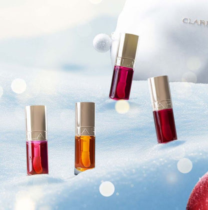 Four lip glosses in different colors on a snowy background with a blurred CLARINS logo.