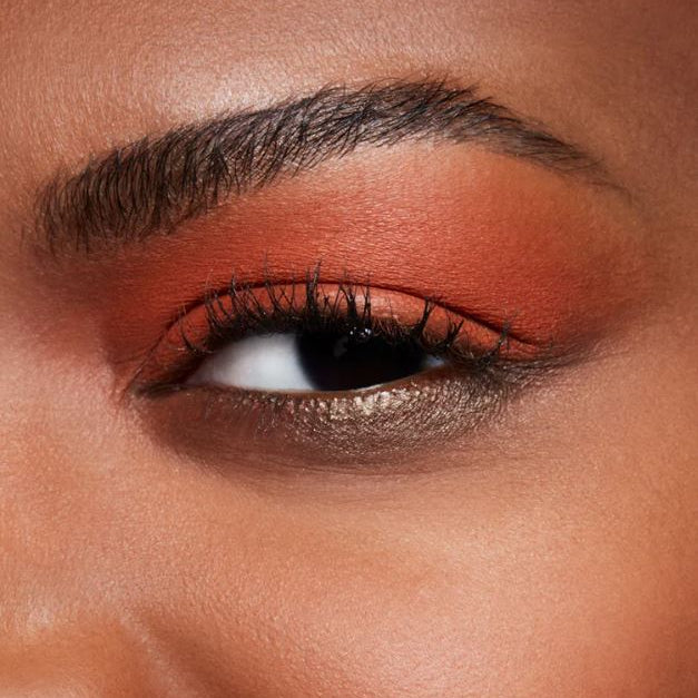 Close-up of a person's eye with orange eyeshadow and long black eyelashes.