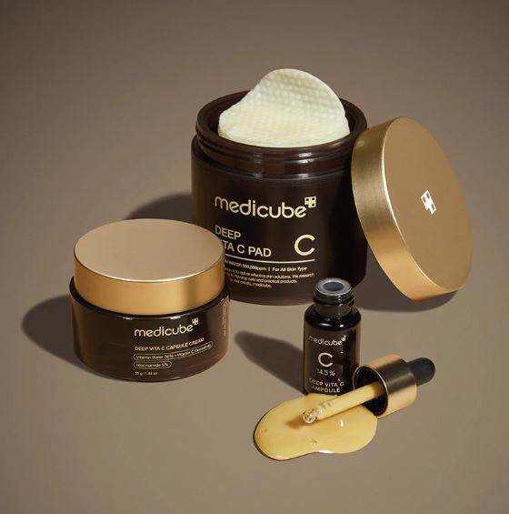 Medicube skincare products including cream jars, a dropper, and a cotton pad on a brown background
