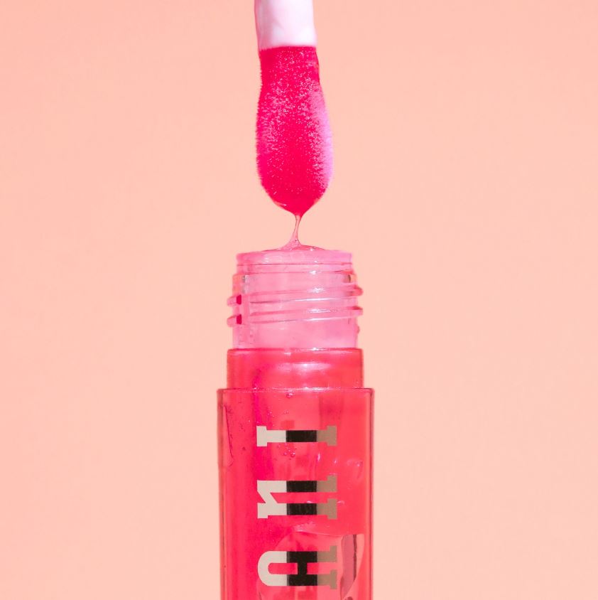 Pink lip gloss with a visible brand name on a peach background