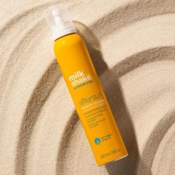 Orange spray bottle labeled 'milk shake sun care' on sand