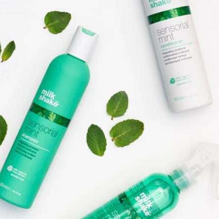 Three bottles of milk_shake sensory mint hair care products on a white background with green leaves.