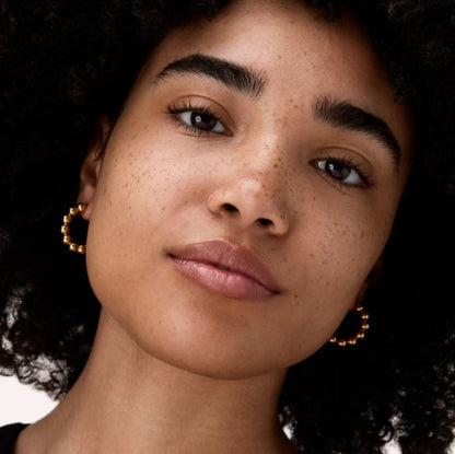 Close-up of a woman wearing gold hoop earrings with a dark background