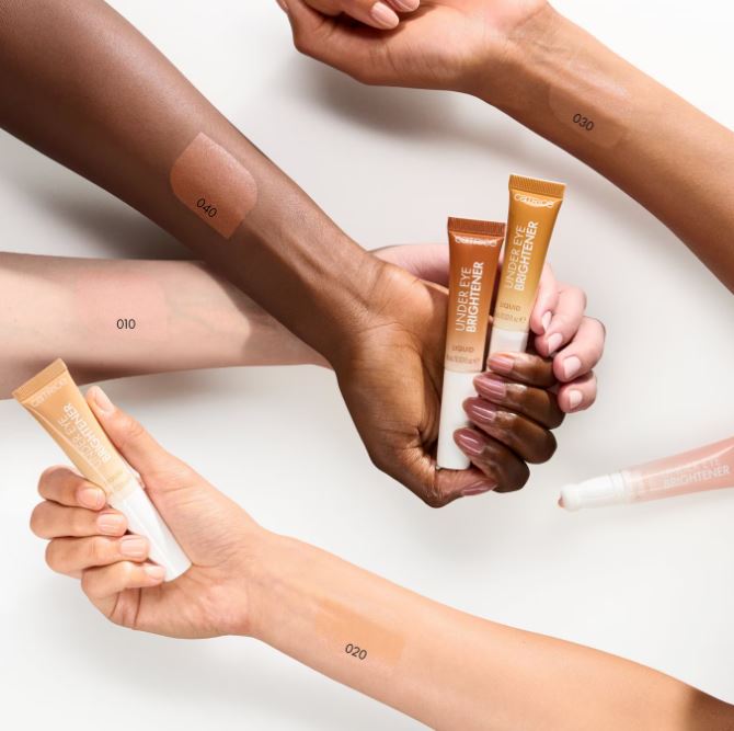 Hands holding tubes of Under Eye Brightener with visible application on skin