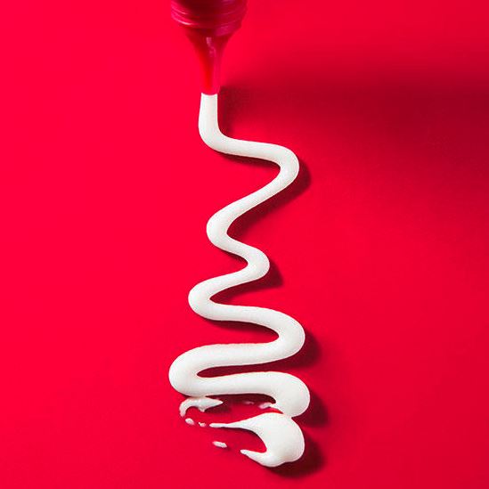 White cream being squeezed from a red tube on a red background