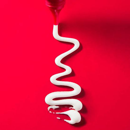 White cream being squeezed from a red tube on a red background