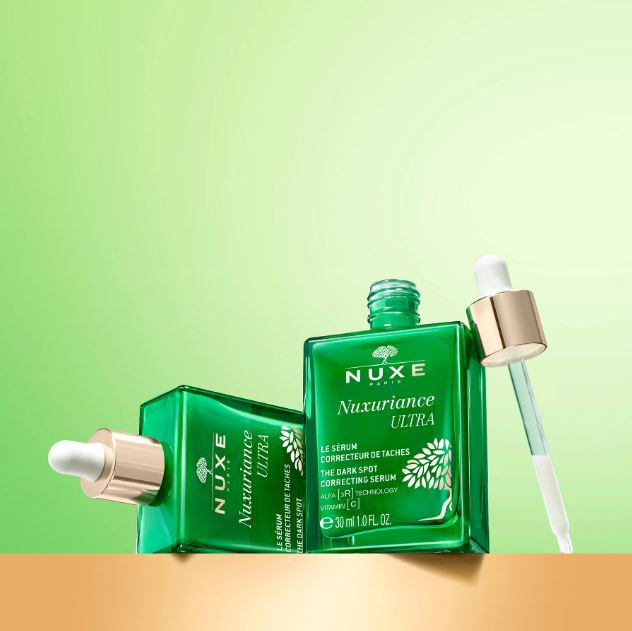 Nuxe Nuxuriance Ultra serum bottles with dropper on a gradient green and orange background